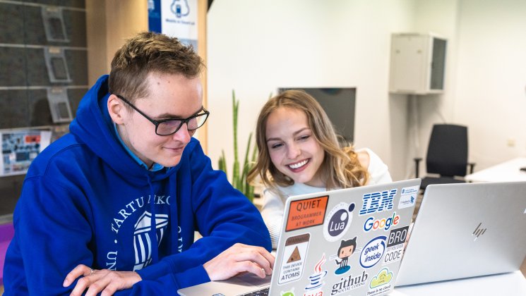 Kaks Tartu Ülikooli tudengit vaatavad sülearvutit ja naeratavad.